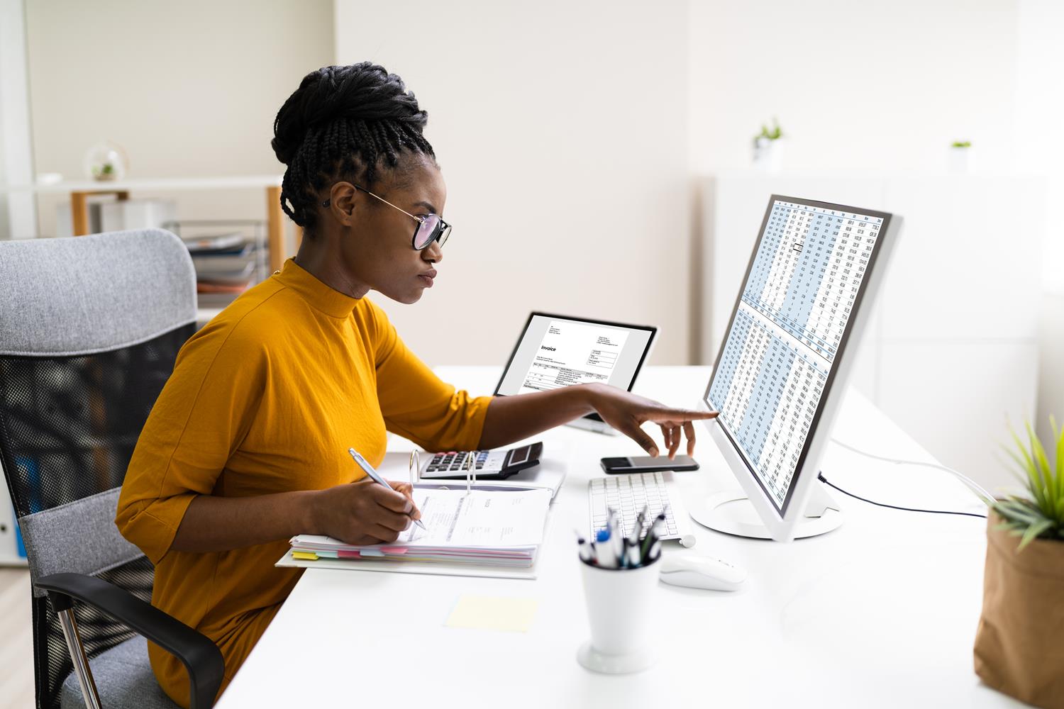 Woman sitting at a desk in front of a screen showing a spreadsheet.