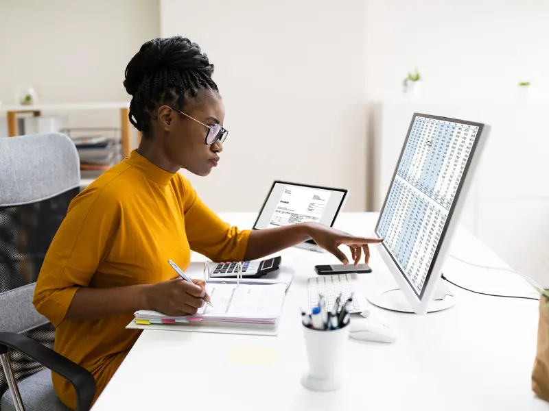 Woman sitting at a desk in front of a screen showing a spreadsheet.