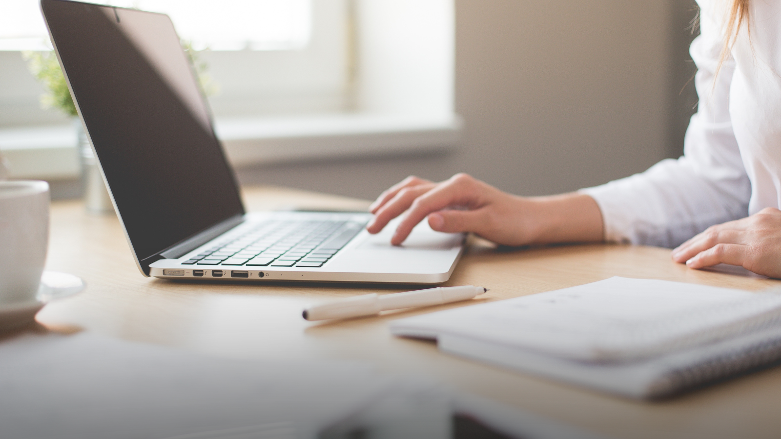 Hand reaching to a laptop on a desk with notebook and pen.