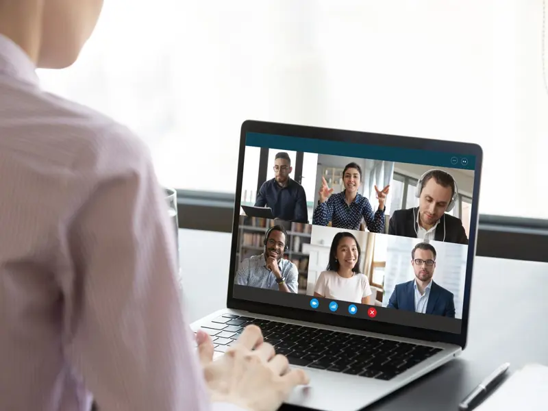 A laptop showing faces on a virtual meeting.