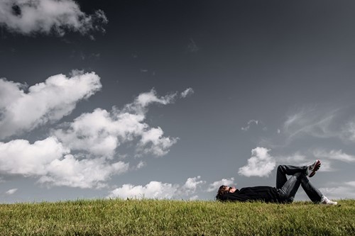 A person lying on a grassy hill above him is a blue sky.