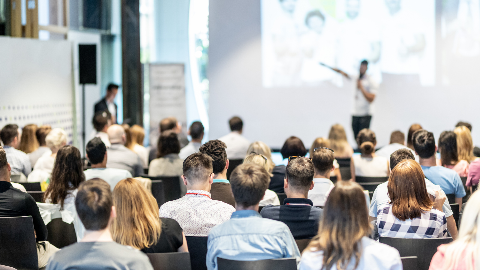 Corporate event showing people sitting listening to a man delivering a presentation.