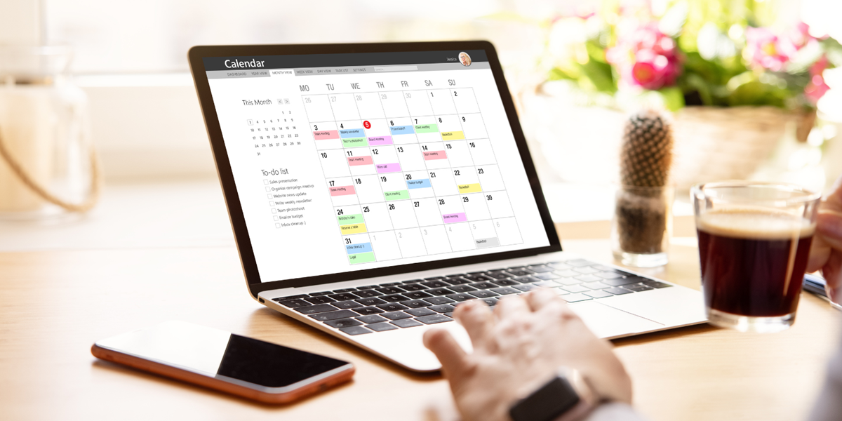 Hand reaching over to a laptop. On the laptop screen is a calendar.