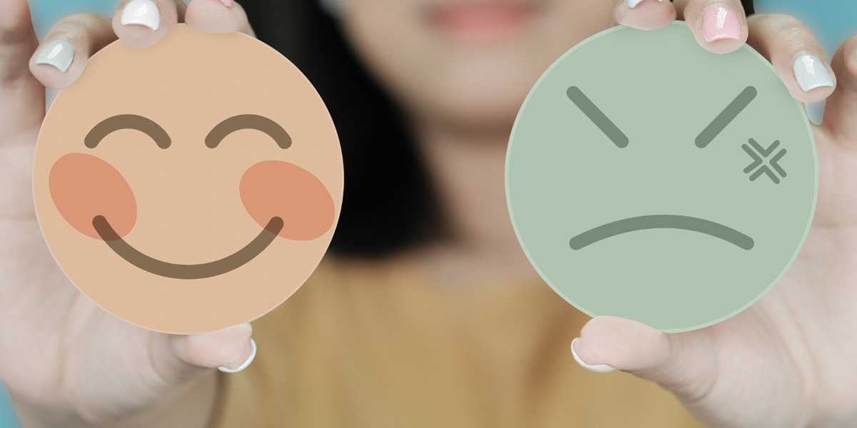 Woman holding an angry face in one hand and a happy face in the other.