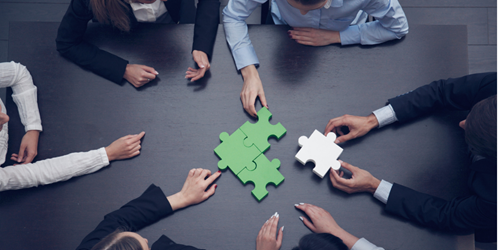 Hands piecing together a puzzle. The puzzle pieces are green with the piece about to complete the puzzle coloured white.