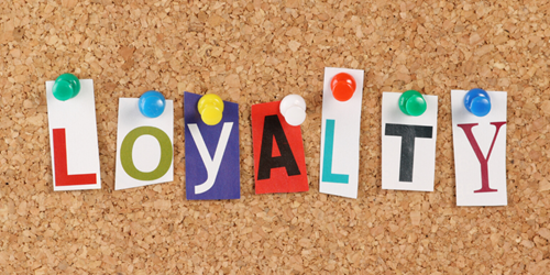 A cork board with individual letters pinned to it. The letters together form the word 'loyalty'.